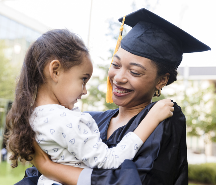 Image of a woman in a cap and gown holding a young child in her arms, both smiling