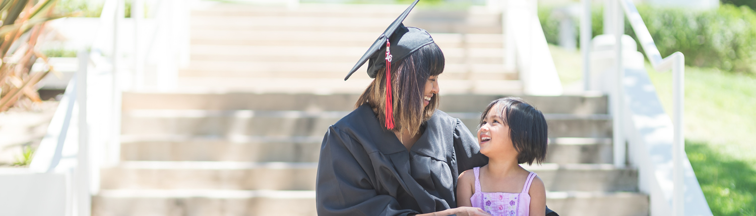 Image of a woman in a cap and gown with a young child sitting on stairs